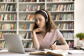 Effective e-learning. Concentrated young female pupil student wear digital earphones interact with...