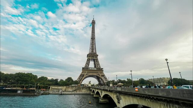The Eiffel Tower stands majestically over the Seine River, framed by a dynamic cloud-filled sky. The scene captures the essence of Paris, showcasing its architectural beauty and vibrant atmosphere.