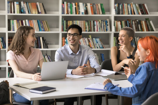 Getting knowledge can be funny. Millennial female students teammates group work on educational project at library together laugh on young male leader joke having fun at studying discuss amusing fact