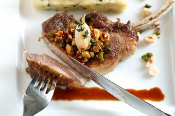 Gourmet lamb chop with nuts and herbs on a white plate, garnished with a savory sauce.