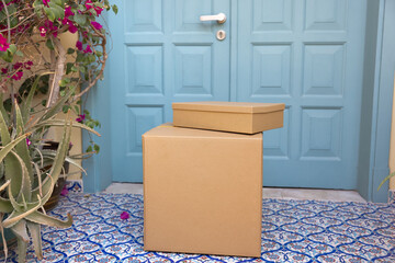 Stack of small and large postal cardboard boxes carried by courier and left at front door of house,...
