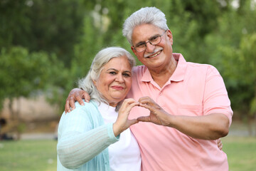 Indian happy senior couple making and showing heart with hands in garden