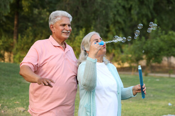 Indian happy Senior couple playing bubbles in garden