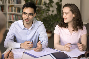 Knowledge sharing. Smiling teen female international college university student take part in group conversation at library listen to young male groupmate in glasses speaking proposing idea to discuss