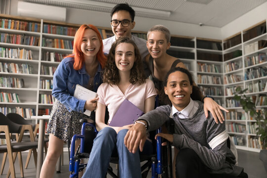 Happy diverse team successful motivated college pupils university students including teenage girl wheelchair user gather in library for group portrait hug laugh enjoy unity bonding friendly relations