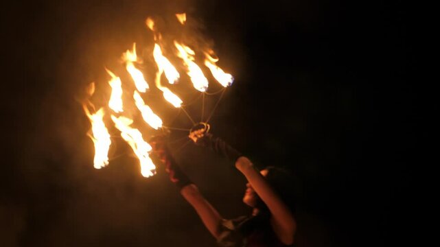 A circus woman with burning torches in her hands on a black background, the performance of artists with fire. A woman holds torches with fire and rotates them in a circle.