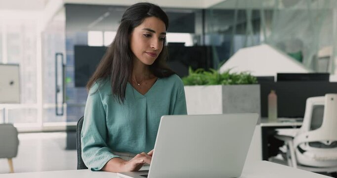 Focused businesswoman, corporate staff member using laptop seated at desk in modern workspace, review received document, prepare report, responding on business mails, browsing internet for information