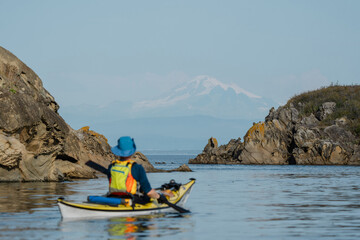 Woman kayaking along Sucia Island in the San Juan Islands in the Pacific Northwest in Washington with Mt Baker in background