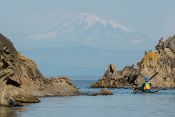 Woman kayaking along Sucia Island in the San Juan Islands in the Pacific Northwest in Washington with Mt Baker in background