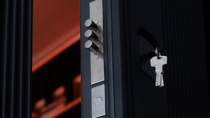 Extended door lock bolts and keys in the keyhole of an open black armored entrance door. Opening...