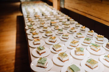 Rows of plated desserts with green and orange garnishes neatly arranged on a table in a well-lit banquet setting..