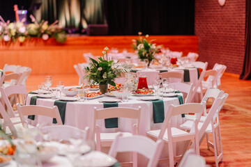 Close-up of an elegant table setup with floral centerpiece, plates, glasses, and food dishes in a decorated banquet hall..
