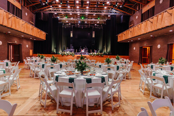 Elegant event hall with round tables, floral centerpieces, and a stage setup for a performance, creating a festive and sophisticated atmosphere.