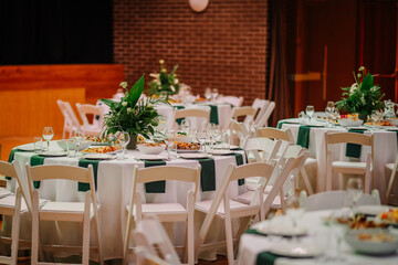 Elegant banquet tables set with white linens, green accents, floral centerpieces, and plates of food in a stylish indoor event setting.