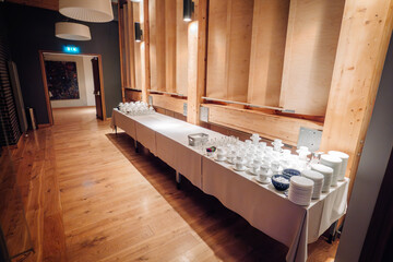 A long table with neatly arranged cups, plates, and glassware in a modern interior, ready for an event or gathering.