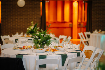  Elegant banquet table setup with white tablecloth, green accents, floral centerpiece, and dishes, in a warmly lit event venue.