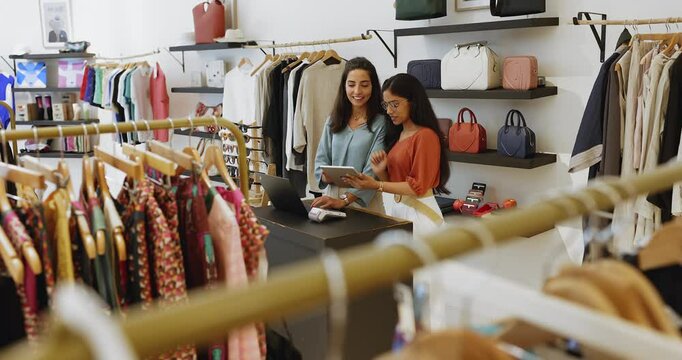 Two women, fashion clothes sellers talking standing at cash desk, using digital tablet, analyze sales data, check stock levels, organizing inventory records, discuss special offers for shop customers