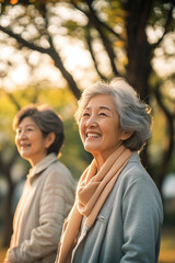 Fototapeta premium A portrait of two happy senior Asian women walking in the park, with sunlight filtering through the trees. 