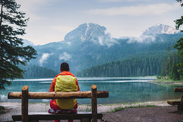 Male traveler with backpack in bright orange jacket on background of Black Lake, Durmitor Park...