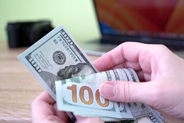 Hand counting dollars money cash on laptop and digital camera background