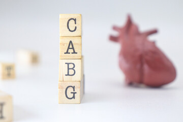 Coronary Artery Bypass Graft acronym. CABG letters written on wooden cubes isolated with a heart on white background with copy space. Surgical procedure on blood