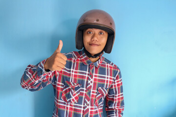 Young Asian man wearing motorbike helmet giving "thumb up" fingers sign