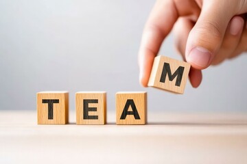 Naklejka premium A hand holds a wooden block depicting the letter M to complete the word TEAM, representing collaboration, unity, and teamwork in a professional or educational setting.