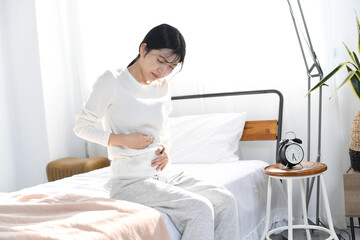 ベッドの上でお腹を抑える若いアジア人女性