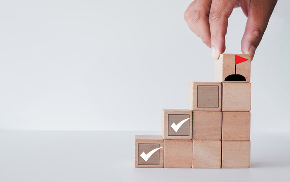Goals achievement,personal growth,work in progress,strategic planning and focus concept.,Hand putting wooden cube with flag icon symbolizing growth, and achievement.