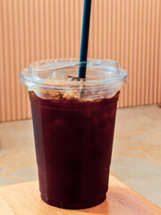 Refreshing Iced Coffee in a Clear Plastic Cup with Straw on Wooden Table Against Minimalist Background.