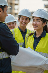 A group of construction Asian workers are smiling and laughing together. One of the workers is holding a piece of project drawings