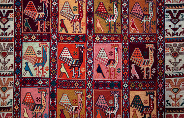 Traditional rug with intricate geometric patterns in red, orange, yellow, pink, and black. Symmetrical shapes and vibrant colors create a rich tapestry design, bordered by bold, contrasting edges.