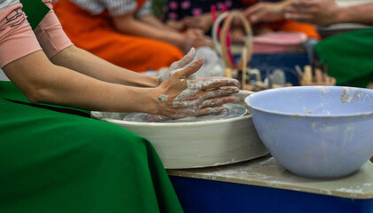 A person wearing a green apron with hands covered in clay is shaping a piece of pottery on a spinning wheel. Fully engaged in the creative process with a focus on the clay piece.