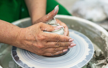 Hands shaping a clay vessel on a pottery wheel, surrounded by a messy workspace. The focus is on the craft and precision, highlighting the art of pottery making in a serene, creative environment.
