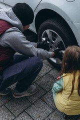 A daughter helps her father change tires on the car, sharing a bonding moment during the task