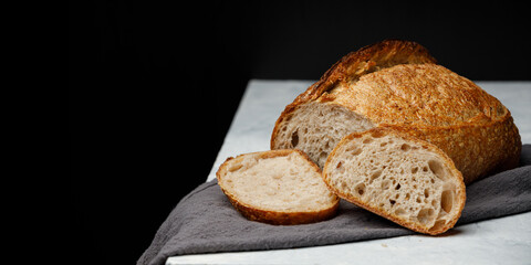Rustic sourdough bread with cut slices on a white table. Panorama, black background with free space for text.