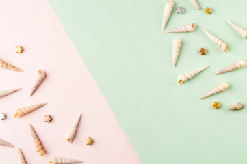 Spiral shells and charms on pastel pink and green background. Pastel flat lay featuring spiral shells and charms.