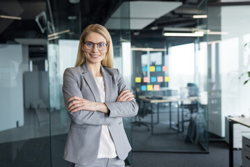 Obraz premium Portrait of confident successful woman inside office at workplace. Businesswoman in business suit with crossed arms smiling and looking at camera.