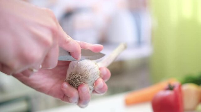 close up of unrecognizable male hands chopping garlic on board. Man's hands cutting garlic with a knife over cutting board. Making food at home, homemade