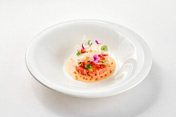 A gourmet dish featuring a delicate piece of salmon tartare, surrounded by a vibrant arrangement of fresh vegetables and edible flowers.