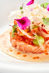A gourmet dish featuring a delicate piece of salmon tartare, surrounded by a vibrant arrangement of fresh vegetables and edible flowers.