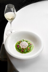 Dish featuring a delicate piece of fish, surrounded by a vibrant arrangement of fresh vegetables and edible flowers. The plate is garnished green sauc
