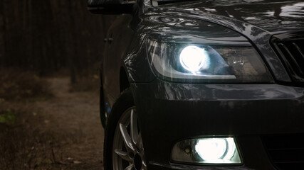 headlight of modern prestigious car. beautiful headlights of a car. dark color. part of the front. glowing headlight, illuminates on a sports car. closeup. light, in the dark