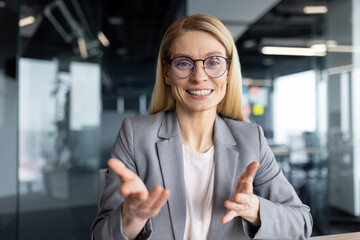 Businesswoman smiling and gesturing talking looking at camera, woman working in office using laptop...