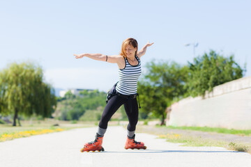 An active young woman rollerblading outdoors in a park, wearing a striped tank top and black...