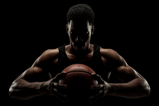 Basketball player holding a ball against black background. Serious concentrated african american man.