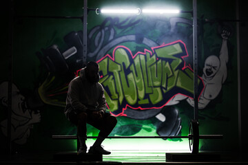 Silhouetted athlete resting in a gym with vibrant graffiti background