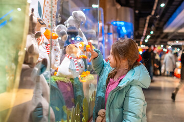 A girl looks at a toy store window.