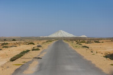 Scenic view of a long road leading to a majestic mountain in a desert landscape under a clear blue sky