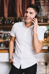Happy man speaking on smartphone while standing at bar counter